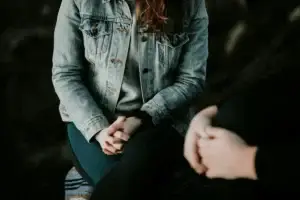 Woman in a denim jacket sitting across from another person with folded hands, in conversation